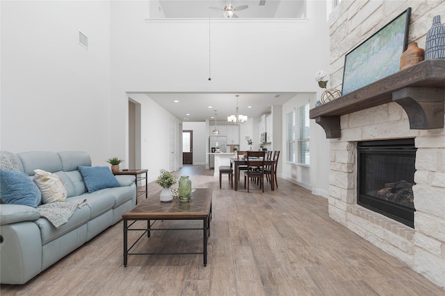564 Embargo Dr, Fate, TX 75189 - living area with a high ceiling, a stone fireplace, light wood finished floors, and ceiling fan with notable chandelier