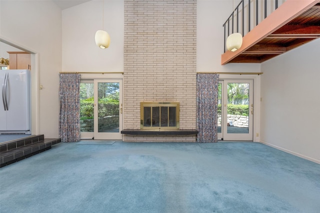 unfurnished living room with beamed ceiling, carpet flooring, a brick fireplace, and a towering ceiling