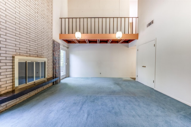 unfurnished living room with visible vents, a fireplace, carpet flooring, and a towering ceiling