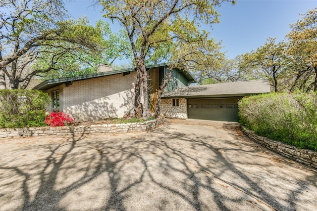 view of front of house featuring concrete driveway, an attached garage, a chimney, and stone siding