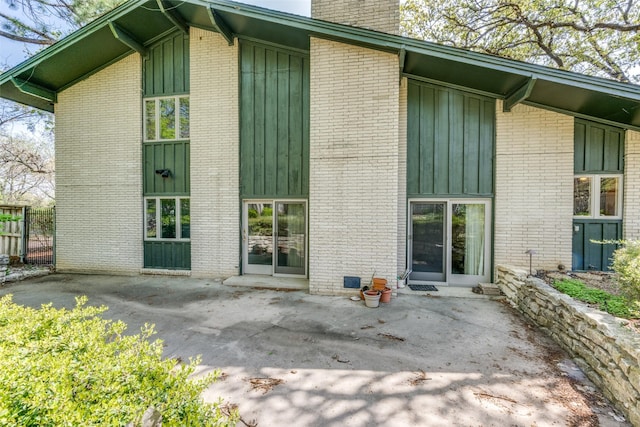 back of house featuring fence, board and batten siding, a patio, and a chimney