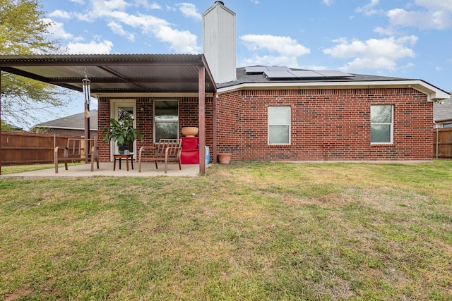 rear view of property with a chimney, a patio area, solar panels, brick siding, and a fenced backyard