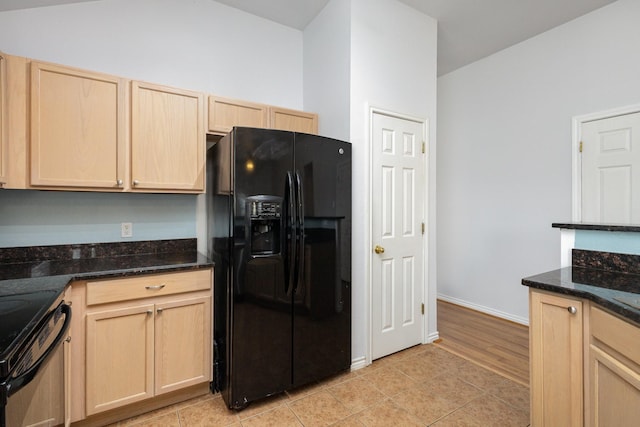 kitchen with light brown cabinetry, black appliances, light tile patterned flooring, and dark stone counters