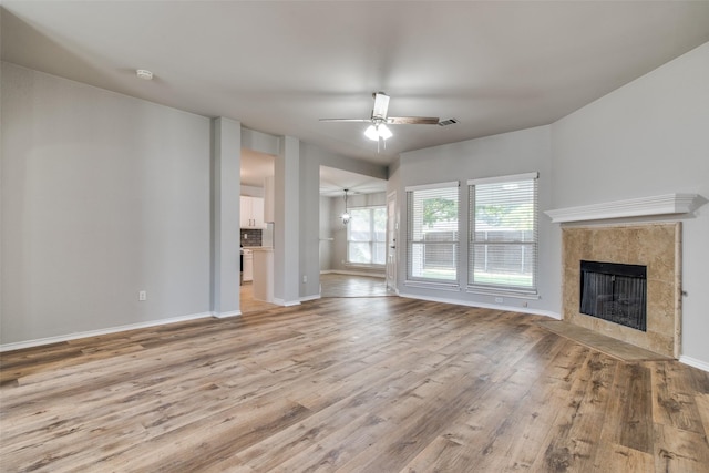 unfurnished living room with baseboards, ceiling fan, light wood-type flooring, and a tile fireplace
