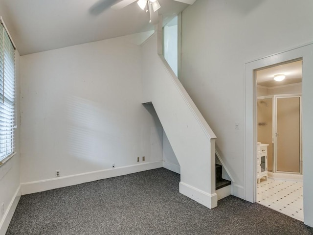 unfurnished living room with baseboards, stairs, dark carpet, and a ceiling fan