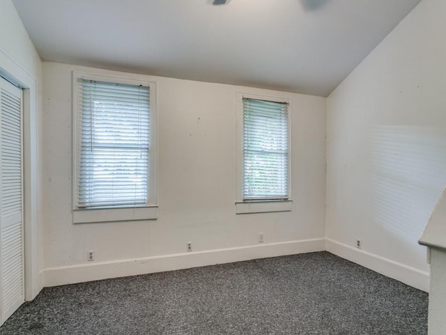 spare room featuring baseboards, lofted ceiling, and dark colored carpet