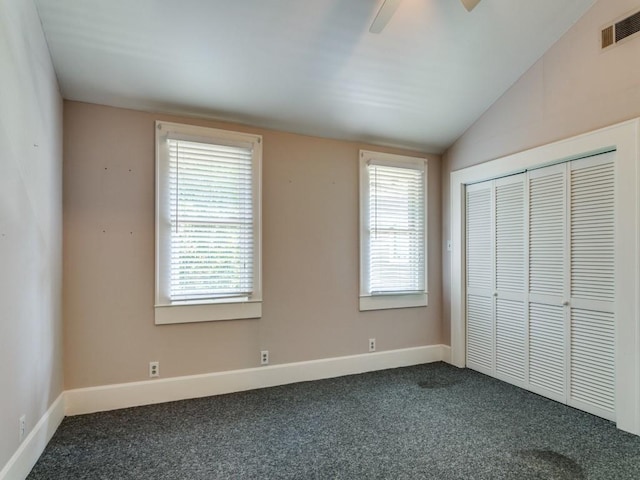 unfurnished bedroom featuring visible vents, vaulted ceiling, multiple windows, and dark colored carpet