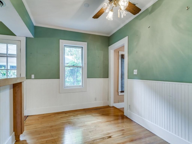 unfurnished room with wainscoting, wood finished floors, ceiling fan, and ornamental molding