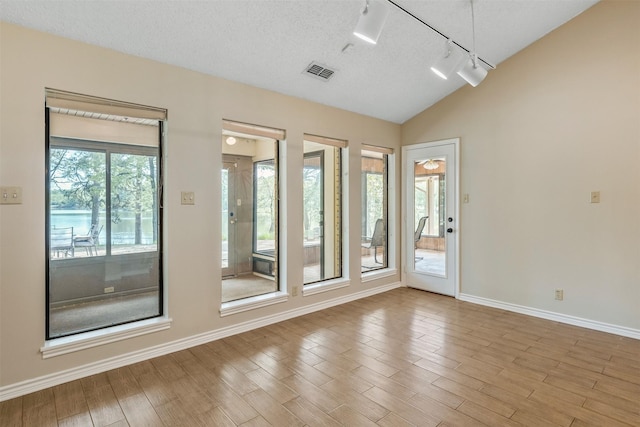 empty room with wood finished floors, baseboards, vaulted ceiling, and track lighting