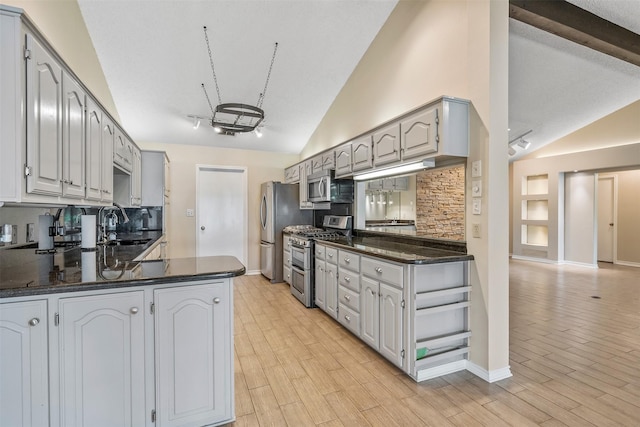 kitchen featuring tasteful backsplash, a peninsula, appliances with stainless steel finishes, a sink, and baseboards