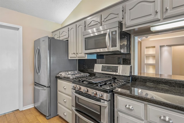 kitchen featuring dark stone countertops, light wood-type flooring, appliances with stainless steel finishes, a textured ceiling, and lofted ceiling