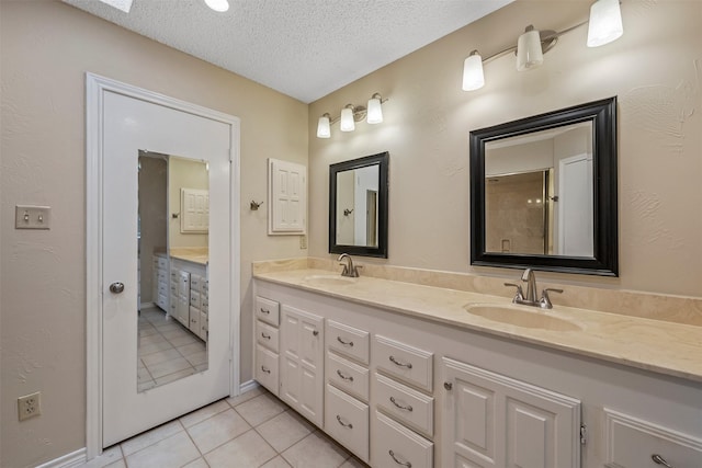 bathroom with a textured ceiling, double vanity, a sink, and tile patterned flooring