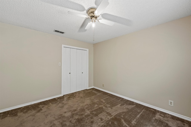 unfurnished bedroom featuring dark carpet, a textured ceiling, a closet, visible vents, and baseboards
