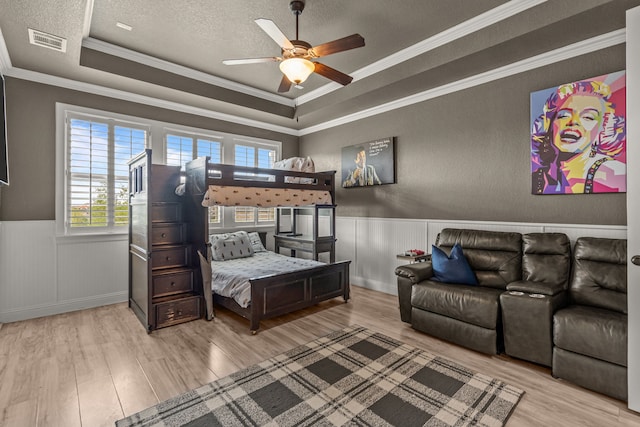 bedroom featuring a tray ceiling, visible vents, wood finished floors, and a wainscoted wall