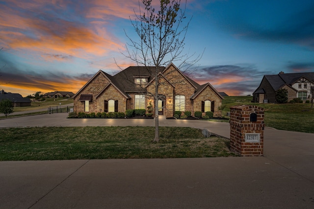 french country style house with stone siding, a lawn, and curved driveway