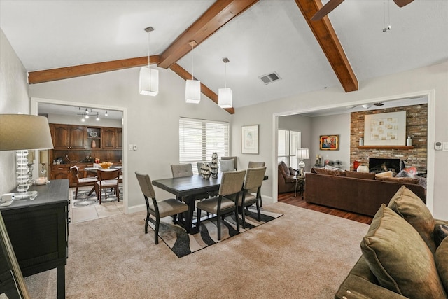 dining area featuring a fireplace, lofted ceiling with beams, light colored carpet, a ceiling fan, and visible vents