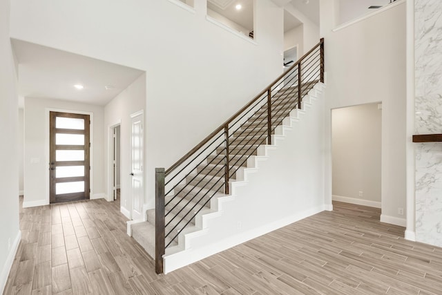 entrance foyer with stairs, light wood-style flooring, baseboards, and a towering ceiling