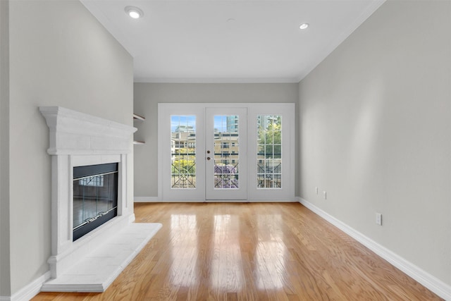unfurnished living room featuring recessed lighting, ornamental molding, baseboards, a glass covered fireplace, and wood finished floors
