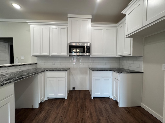 kitchen with dark stone counters, backsplash, stainless steel microwave, and dark wood-style floors