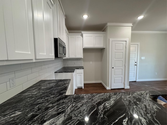 kitchen with crown molding, white cabinetry, stainless steel microwave, dark stone countertops, and backsplash