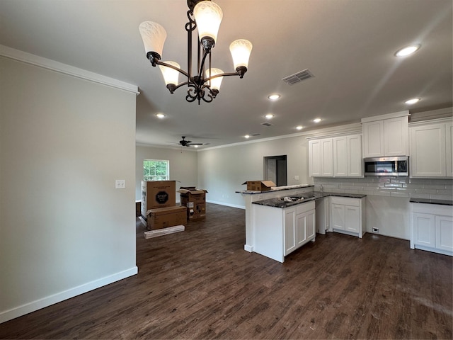 kitchen with white cabinetry, stainless steel microwave, baseboards, visible vents, and ornamental molding
