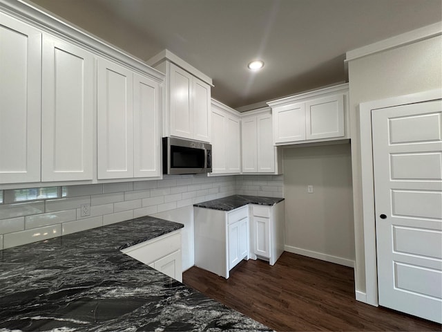 kitchen with dark wood-style flooring, stainless steel microwave, white cabinets, tasteful backsplash, and dark stone countertops