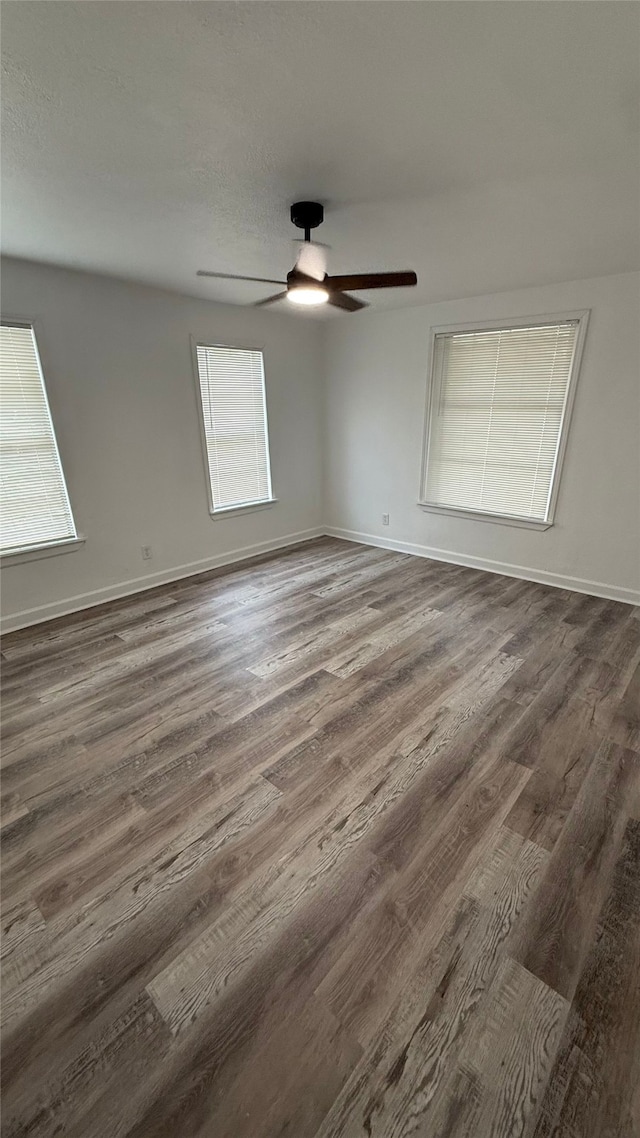 empty room with a ceiling fan, baseboards, and dark wood-style flooring