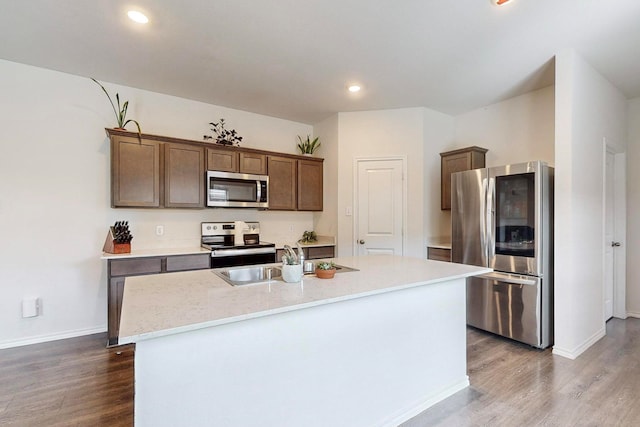 kitchen featuring a center island with sink, a sink, stainless steel appliances, and wood finished floors