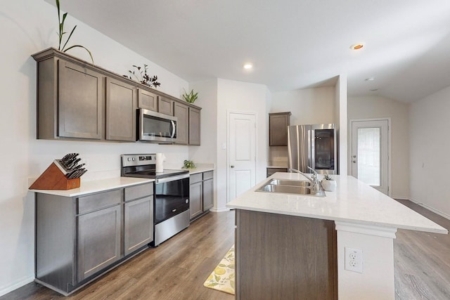 kitchen with light countertops, wood finished floors, stainless steel appliances, an island with sink, and a sink