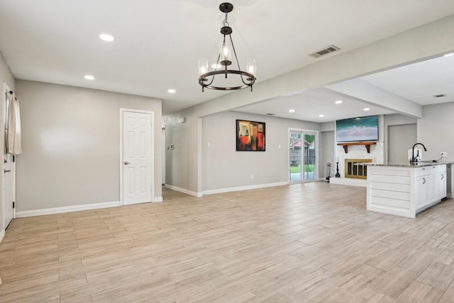 unfurnished living room featuring recessed lighting, a sink, a chandelier, light wood finished floors, and baseboards