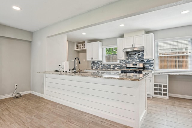 kitchen with stainless steel stove, under cabinet range hood, a sink, a peninsula, and decorative backsplash
