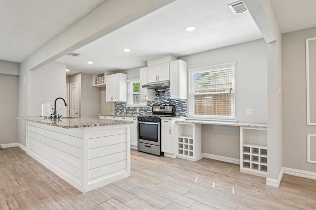 kitchen with gas range, under cabinet range hood, a sink, light stone counters, and baseboards