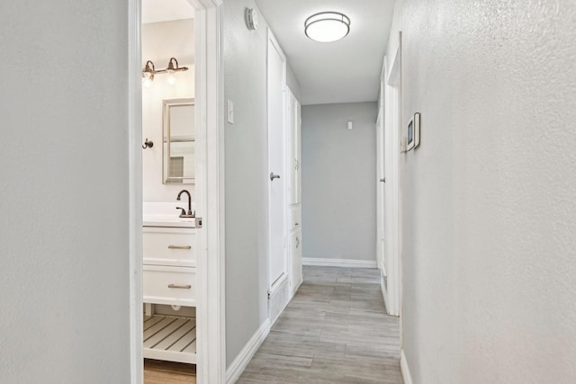 corridor featuring light wood-style floors, baseboards, and a sink