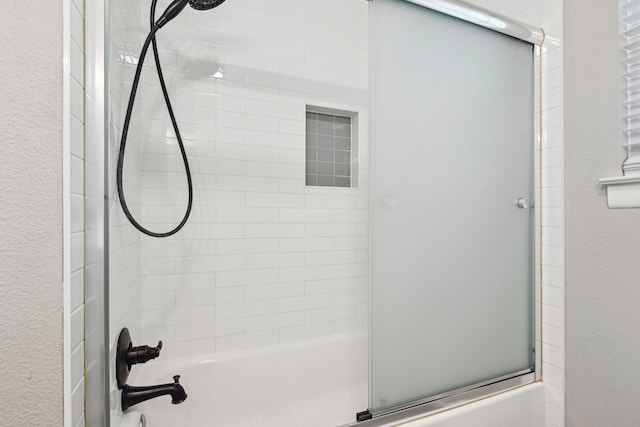 full bath featuring bath / shower combo with glass door and a textured wall