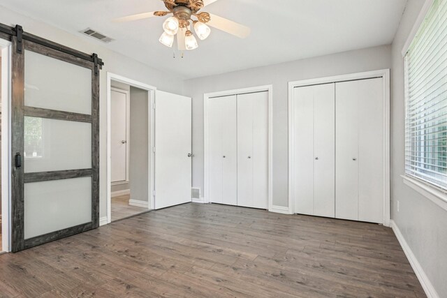 unfurnished bedroom with multiple closets, a barn door, wood finished floors, baseboards, and a ceiling fan