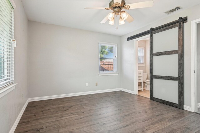 unfurnished room featuring a barn door, dark wood finished floors, ceiling fan, and baseboards
