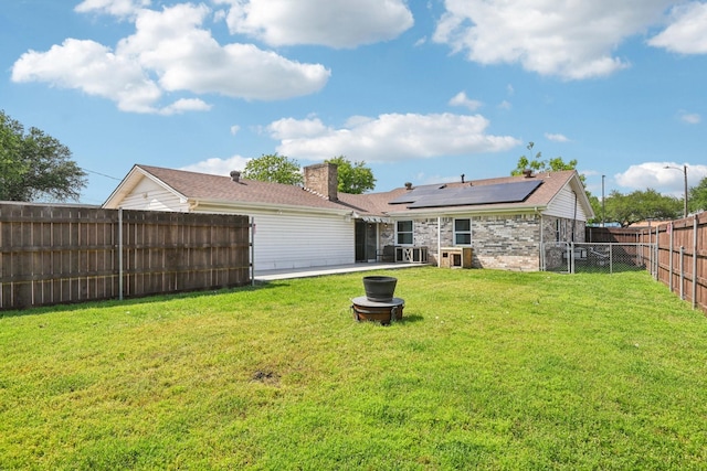 rear view of house with roof mounted solar panels, a chimney, and a patio area
