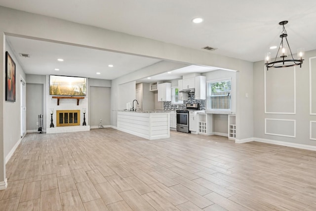 kitchen with stainless steel range with gas cooktop, open floor plan, white cabinetry, a chandelier, and a fireplace