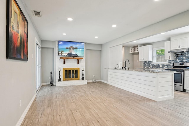 kitchen featuring stainless steel gas stove, under cabinet range hood, baseboards, recessed lighting, and a sink