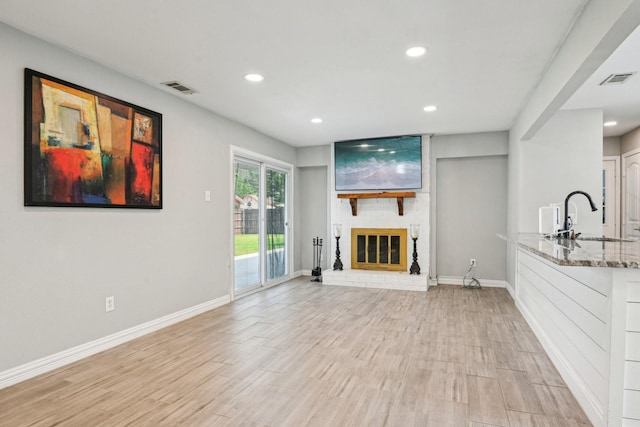 unfurnished living room featuring a sink, recessed lighting, a brick fireplace, baseboards, and light wood-style flooring