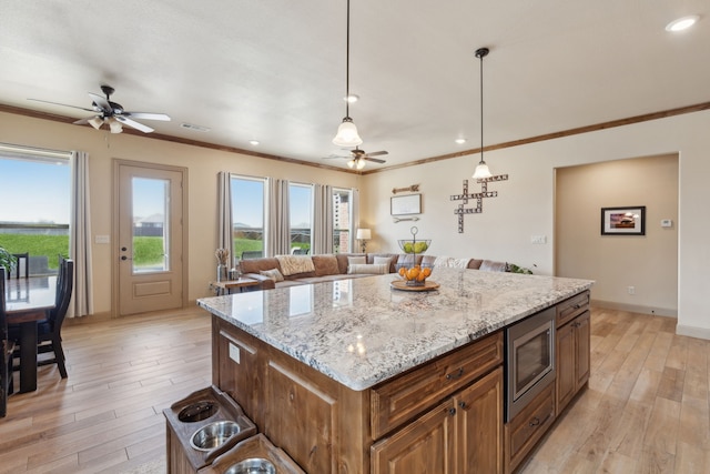 kitchen featuring stainless steel microwave, ornamental molding, light wood finished floors, and ceiling fan