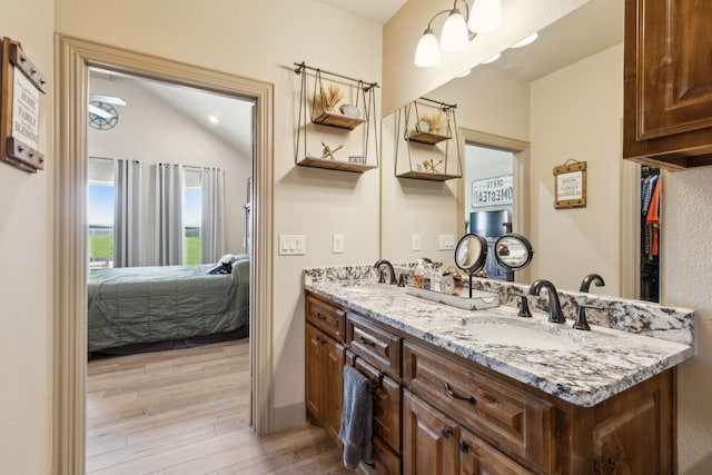 ensuite bathroom featuring wood finished floors, a sink, double vanity, ensuite bath, and lofted ceiling