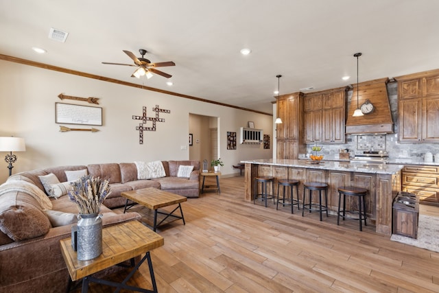 living room featuring light wood-type flooring, a ceiling fan, visible vents, and ornamental molding