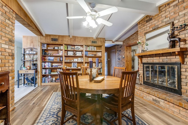 dining room with wood walls, a brick fireplace, wood finished floors, brick wall, and ceiling fan