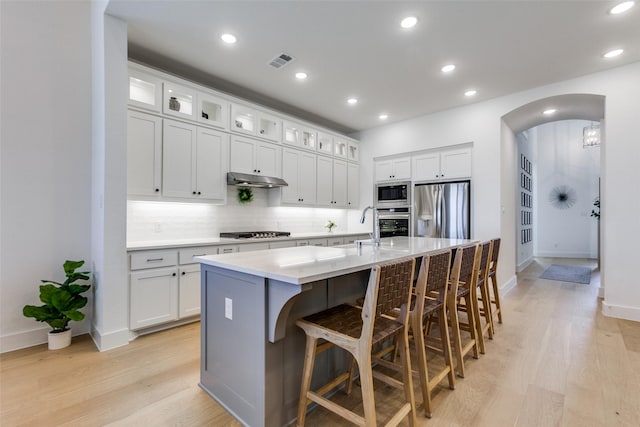 1716 Bradford Pear Way, Celina, TX 75078 - kitchen featuring appliances with stainless steel finishes, light wood-style flooring, backsplash, arched walkways, and a kitchen island with sink