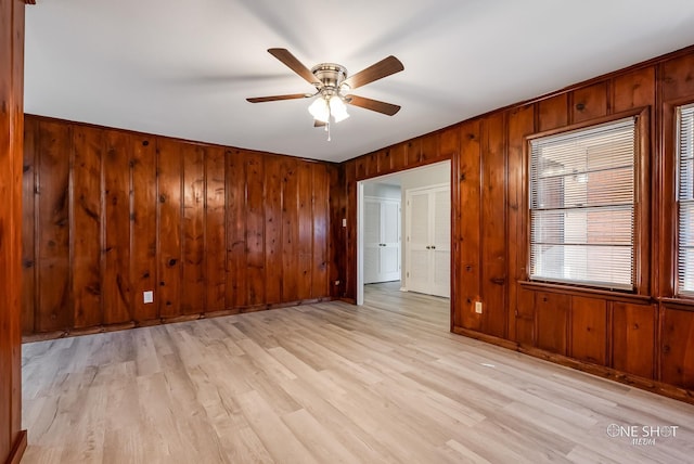spare room with wood walls, a ceiling fan, light wood-style flooring, and baseboards