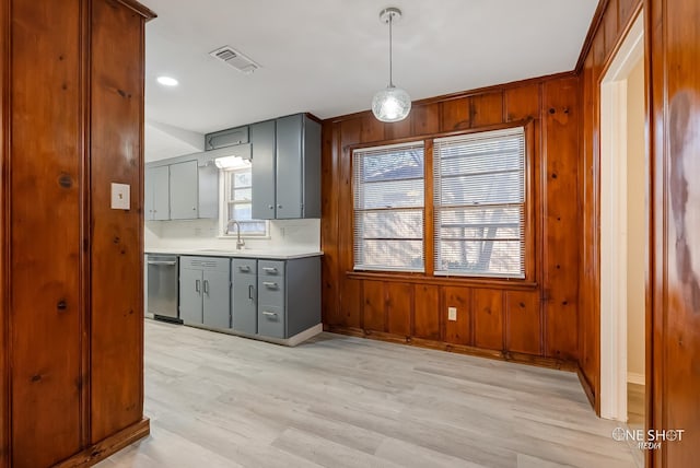 kitchen featuring stainless steel dishwasher, gray cabinets, a sink, light wood-style floors, and light countertops