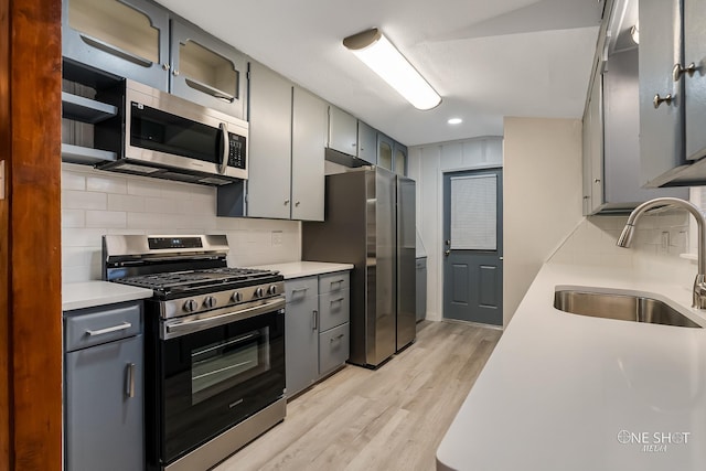 kitchen featuring stainless steel appliances, a sink, light countertops, light wood-style floors, and tasteful backsplash