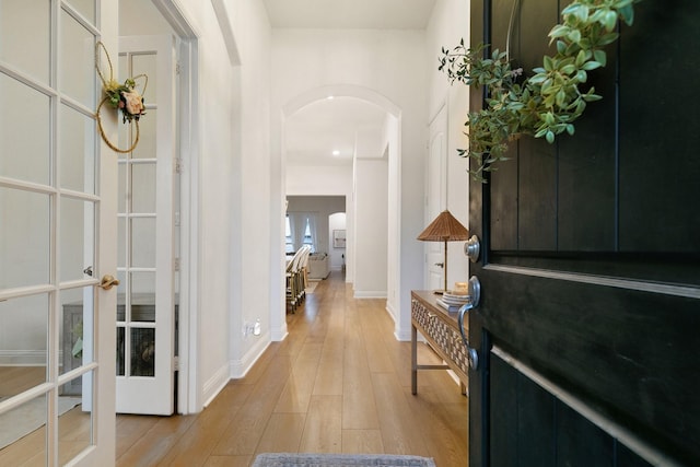 entryway with baseboards, arched walkways, french doors, and light wood finished floors