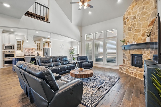 living area with hardwood / wood-style flooring, a ceiling fan, a fireplace, a high ceiling, and recessed lighting